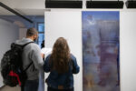 Foto eines Ausstellungsraumes mit abstrakter Malerei. Im Vordergrund sind Besucher*innen zu erkennen.