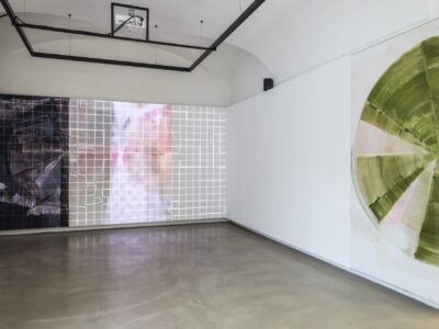 Foto eines Ausstellungsraumes mit zwei abstrakten Malereien. Die Malereien zeigen Halbkreise. Sie werden von einem projizierten Gitternetz überlagert. Die Malerei an der Stirnwand wird von einer Projektion überlagert.