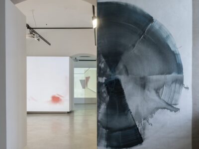 Foto eines Ausstellungsraumes mit abstrakter Malerei. Die Malereien zeigen Halbkreise. Im Hintergrund sind zwei weitere Ausstellungsräume mit abstrakter Malerei und Videoprojektion zu erkennen.