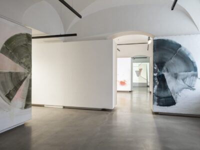 Foto eines Ausstellungsraumes mit abstrakter Malerei. Die Malereien zeigen Halbkreise. Im Hintergrund sind zwei weitere Ausstellungsräume mit abstrakter Malerei und Videoprojektion zu erkennen.