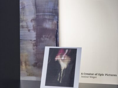 Foto eines Ausstellungsraumes mit abstrakter Malerei durch ein Schaufenster aufgenommen.