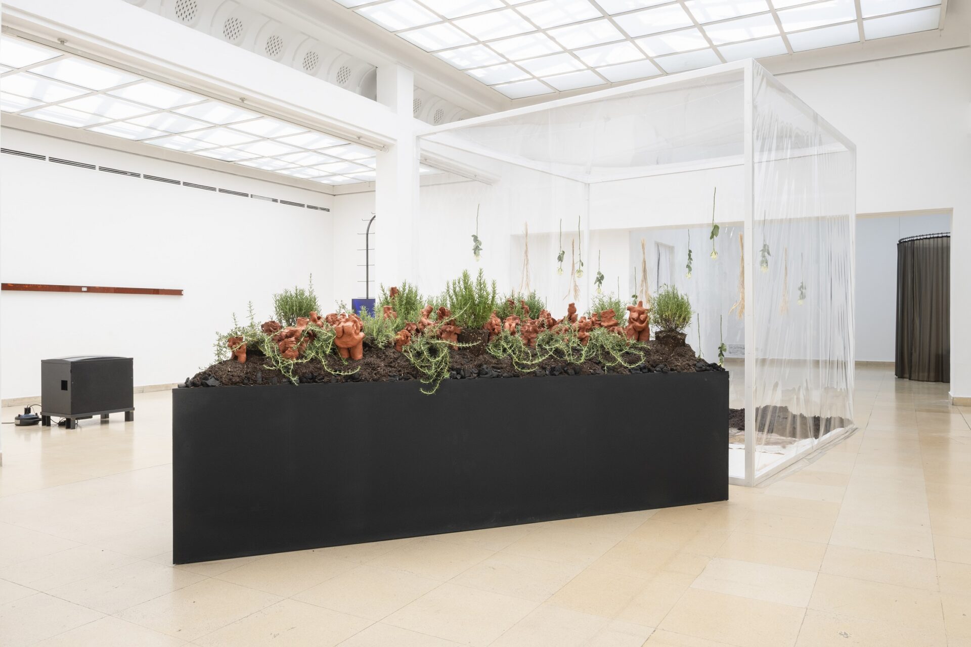 Photo of exhibition space with black objekt and on top terracotta figures and rosmary on earth and charcoal