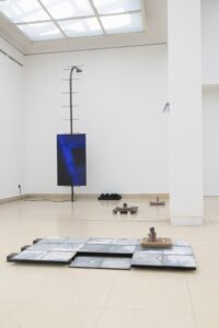 Ausstellungsraum mit Bildschirm aufgehängt an Stahlskulptur und Objekte am Boden