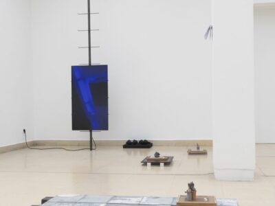 Ausstellungsraum mit Bildschirm aufgehängt an Stahlskulptur und Objekte am Boden