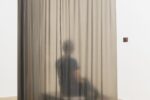 Photo of exhibition space with latex curtain and a person sitting behind with headphones