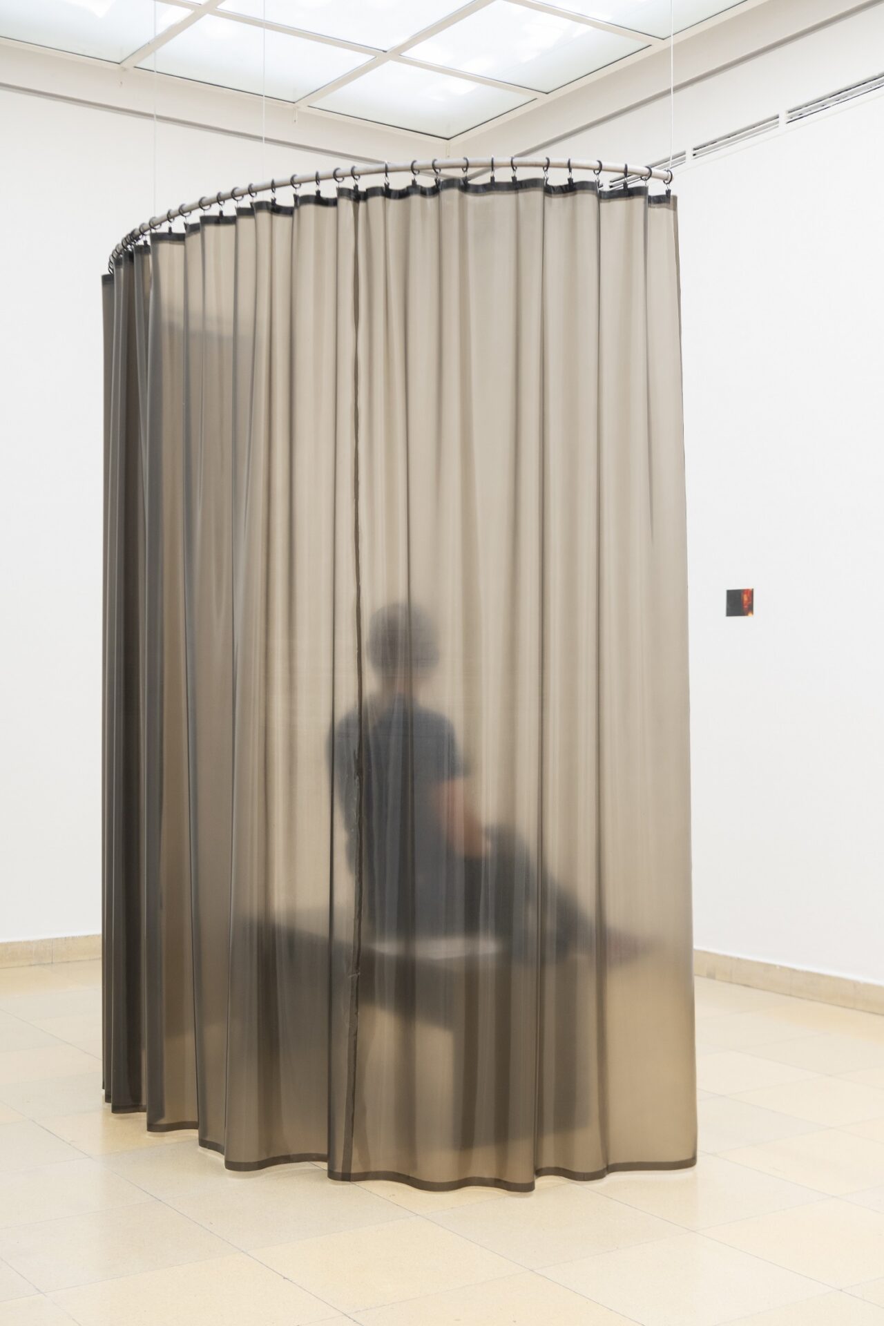 Photo of exhibition space with latex curtain and a person sitting behind with headphones