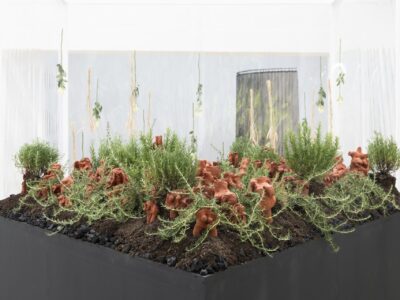 Ausstellungsraum mit schwarzem dreieckigem Beet mit Tonfiguren und Rosmarinpflanzen auf Kohle und Erdebeet