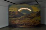 Ausstellungsansicht einem Gemälde aus dem 19 Jahrhundert als Tapete, dass eine gebirgige Landschaft im Sonnenuntergang zeigt; darüber ein Schriftzug in Neonröhren der lautet "Don't Dream Dreams"