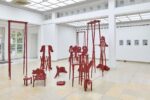 Ausstellungsansicht Kunstpavillon mit rot lackierten Holzskulpturen in unterschiedlichen Größen und Höhen, im Hintergrund Bilder