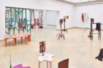 Ausstellungsansicht Kunstpavillon mit unterschiedlich farbig lackierten Holzskulpturen in unterschiedlichen Größen und Höhen mit Fotos und rot lackierten Holzskulpturen in unterschiedlichen Größen und Höhen