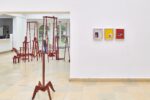 Ausstellungsansicht Kunstpavillon mit rechts drei Collagen an der Wand und unterschiedlich farbig lackierten Holzskulpturen in unterschiedlichen Größen und Höhen mit Fotos