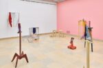 Ausstellungsansicht Kunstpavillon mit unterschiedlich farbig lackierten Holzskulpturen in unterschiedlichen Größen und Höhen mit Fotos und Stoffen und Aluminiumobjekten