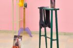 Ausstellungsansicht Kunstpavillon mit unterschiedlich farbig lackierten Holzskulpturen in unterschiedlichen Größen und Höhen mit Fotos und Stoffen vor rosa Wand