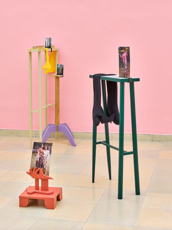Exhibition view Kunspavillon with wooden sculptures painted in different colours, in various sizes and heights, with photographs next to a pink wall