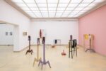 Exhibition view Kunspavillon with wooden sculptures painted in different colours, in various sizes and heights, with photographs next to a pink wall