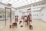 Exhibition view Kunstpavillon with wooden sculptures painted in different colours, in various sizes and heights, with photographs; painted pictures on the right