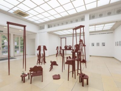 Ausstellungsansicht Kunstpavillon mit rot lackierten Holzskulpturen in unterschiedlichen Größen und Höhen, rechts gemalte Bilder