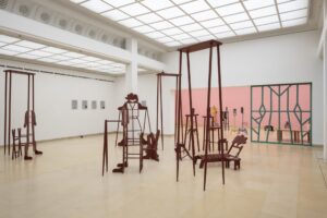 Exhibition view Kunstpavillon with red-painted wooden sculptures in various sizes and heights with figurative objects and painted pictures on the left