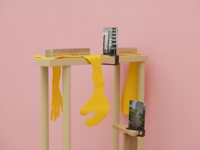 Ausstellungsansicht Kunstpavillon mit Holzobjekten, Fotos und gelbem Stoff die an Hände erinnern
