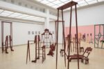 Exhibition view Kunstpavillon with red-painted wooden sculptures in various sizes and heights with figurative objects and painted pictures on the left