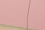 Exhibition view Kunstpavillon with orange/black painted sculpture with metal rod and black fabric in front of pink wall
