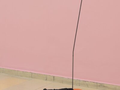 Ausstellungsansicht Kunstpavillon mit orange/schwarz lackierter Skulptur mit Metallstab und schwarzem Stoff vor rosa Wand