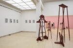 Exhibition view Kunstpavillon with red-painted wooden sculptures in various sizes and heights with figurative objects and painted pictures on the left