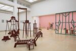 Exhibition view Kunstpavillon with wooden sculptures painted in different colours, in various sizes and heights, with photographs, painted pictures on the left and wooden room dividers in the background.