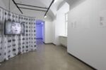 exhibiton view, left there is a curtain with lips on it and a screen with a singing women