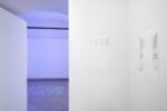 exhbition view, on the right of the picutre there is a dada poem on the wall, in the background blue light