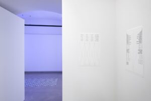 Ausstellungsansicht, rechts sieht man ein grafisches Bild eines phono-poetischen Gedichtes im Hintergrund blasses blaues Licht