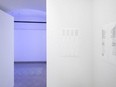 Ausstellungsansicht, rechts sieht man ein grafisches Bild eines phono-poetischen Gedichtes im Hintergrund blasses blaues Licht