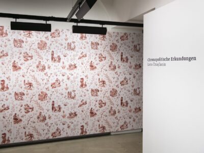 Ausstellungsansicht mit einer rötlichen Taptete mit floralem Muster, zeigt die Arbeit Balkangreuel