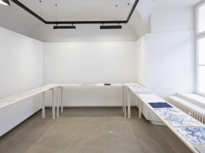 Foto Ausstellung Neue Galerie mit schmalen Tischen und weißen, blauweißen und blauen Blättern darauf