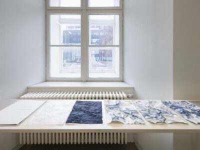 Foto Ausstellung Neue Galerie mit schmalen Tischen und weißen, blauweißen und blauen Blättern darauf