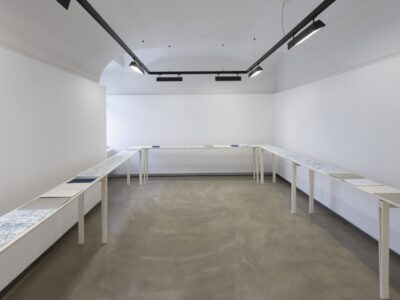 Foto Ausstellung Neue Galerie mit schmalen Tischen und weißen, blauweißen und blauen Blättern darauf