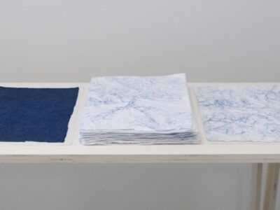 Foto Ausstellung Neue Galerie mit schmalen Tischen und weißen, blauweißen und blauen Blättern darauf