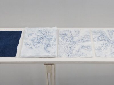 Foto Ausstellung Neue Galerie mit schmalen Tischen und weißen, blauweißen und blauen Blättern darauf