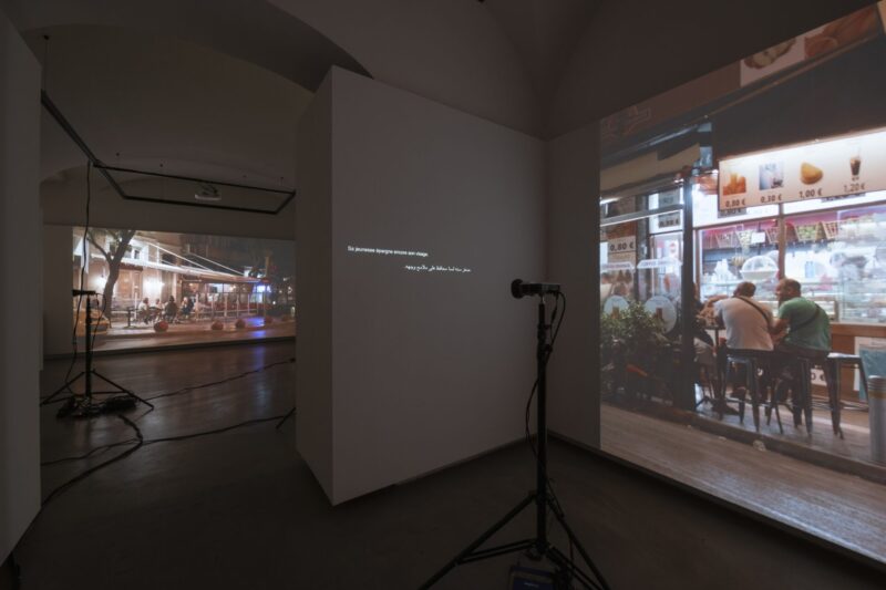 An exhibition space with a video installation can be seen. Images and text are projected onto the walls. The projector is clearly visible in the foreground.
