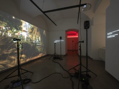Foto Ausstellung mit Video und Text an den Wänden, im HIntergrund rotes Licht