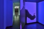 Photo of an exhibition with a video installation and chalk drawings on a black wall in the back room