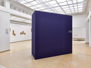 Photo of the exhibition at Kunstpavillon with a blue box in the middle, text on the wall and wooden panels on the left wall