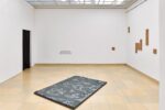 Photo of the exhibition at Kunstpavillon with wooden panels and text on the wall and a fabric on the floor