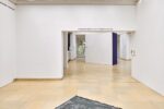 Photo of the exhibition at Kunstpavillon with a text on the wall above the walkthrough and a fabric on the floor