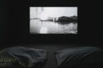Photo of the exhibition at Kunstpavillon with a video installation in a black room, in front two beanbags
