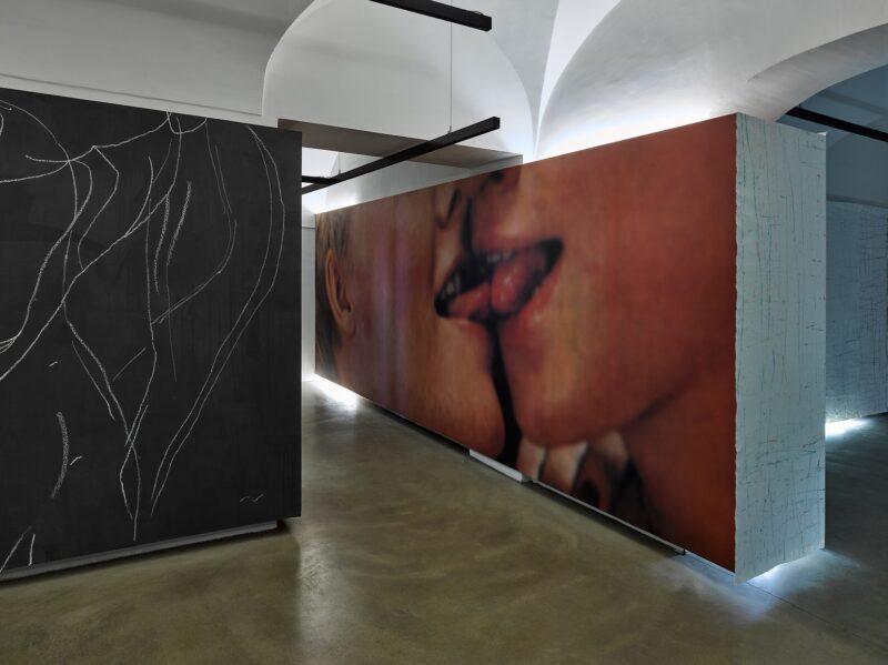 Photo of an exhibition with a video installation and chalk drawings on a black wall in the back room