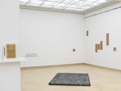 Ausstellungsansicht Kunstpavillon mit Holzpanelen an der Wand, Textil am Boden und Publikation an der Wand lehnend