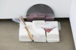 Foto Ausstellung mit Assemblage am Boden mit metallem Kreis, und weißen Packungen mit Stab