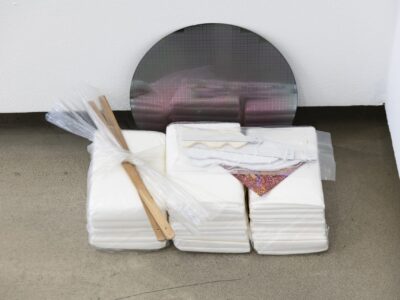 Foto Ausstellung mit Assemblage am Boden mit metallem Kreis, und weißen Packungen mit Stab