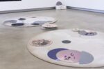 Foto Ausstellung mit Assemblage aus Schaffilz und metallenen Kreisen mit schwarzem Pulver